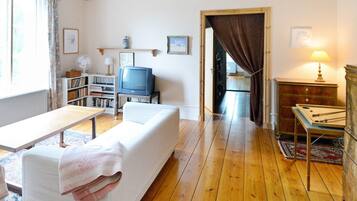 A living room with a sofa, a television, a bookshelf, and a wooden floor.