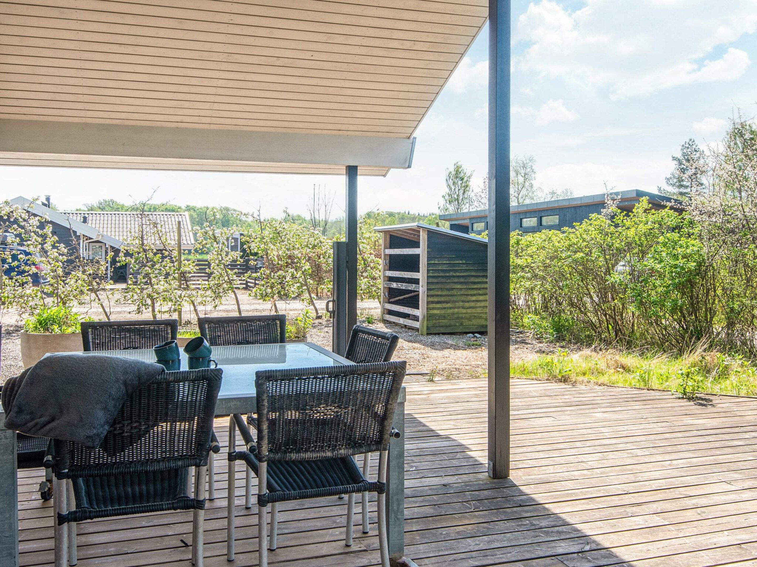 An outdoor patio with a table and chairs, a covered area, and a view of a building and trees.