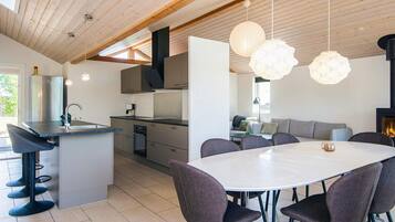 A modern kitchen with a central island, dining area with chairs, and a fireplace.