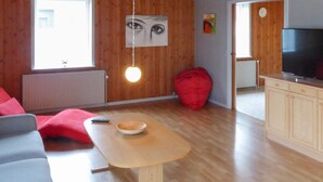 Una sala de estar acogedora con techo de madera, un sillón de peluche rojo, un televisor y una mesa de comedor con un tazón.