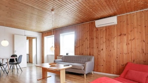 Una sala de estar moderna con techo de madera, un sofá gris, una mesa de comedor de madera y un cojín rojo.