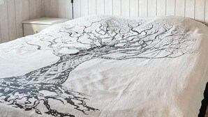 Ein Bett mit weißer Bettdecke und einem schwarzen Baum-Motiv.