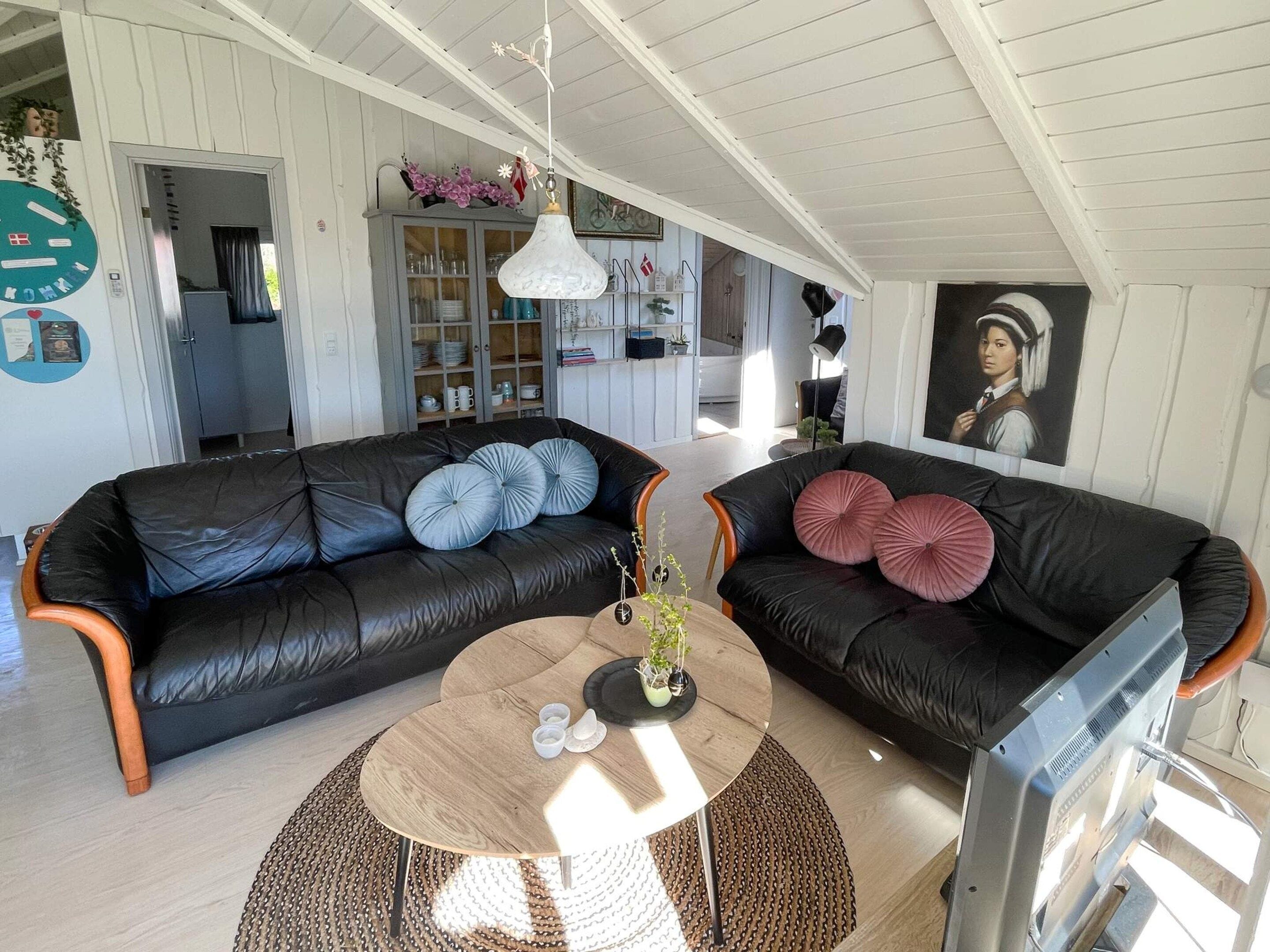 A living room with two black leather sofas, a round wooden coffee table, and a television.