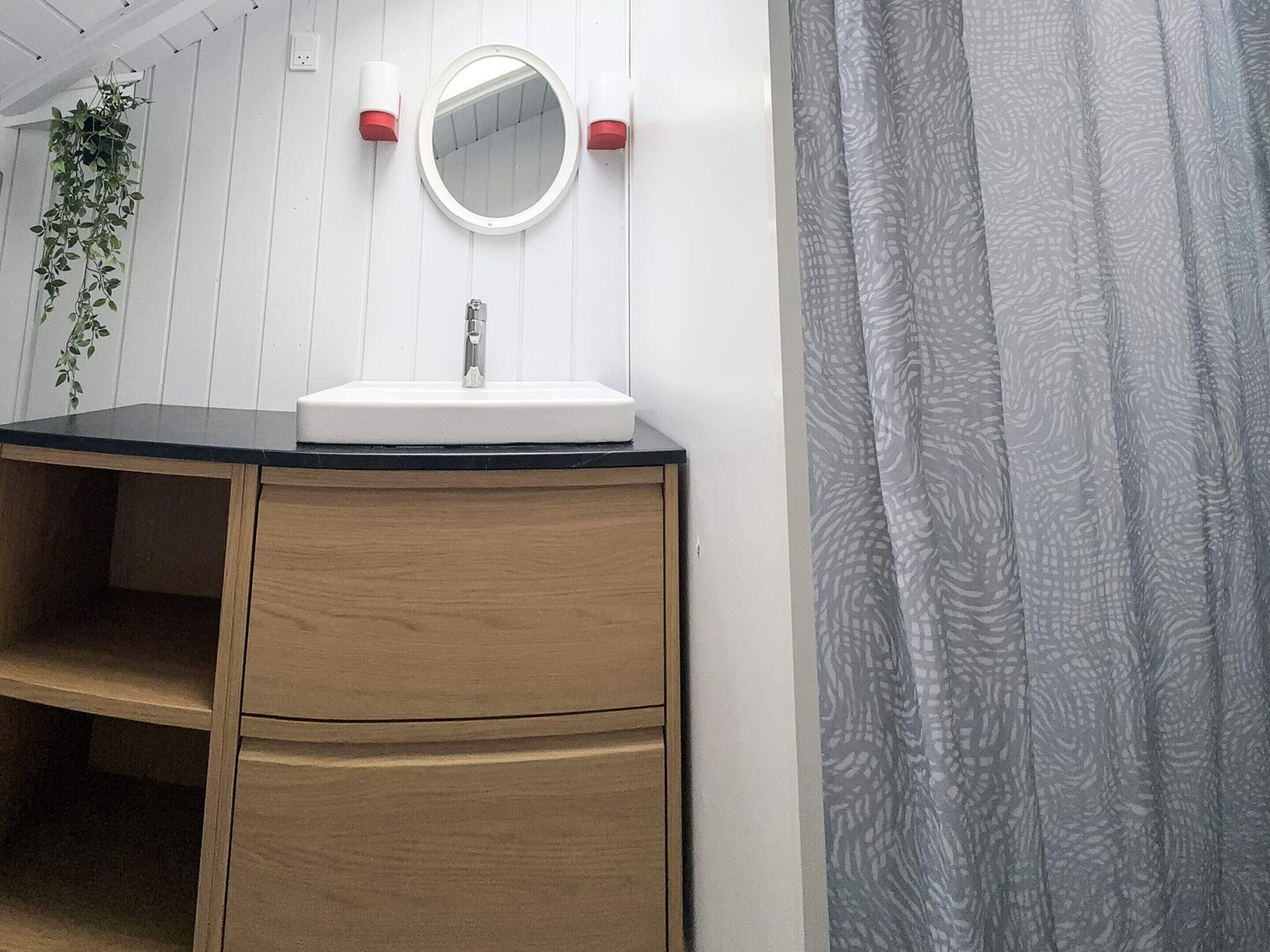 Ein Badezimmer mit einem weißen Waschbecken, einem Holz-Badmöbel, einem Spiegel und roten Seifenspendern.