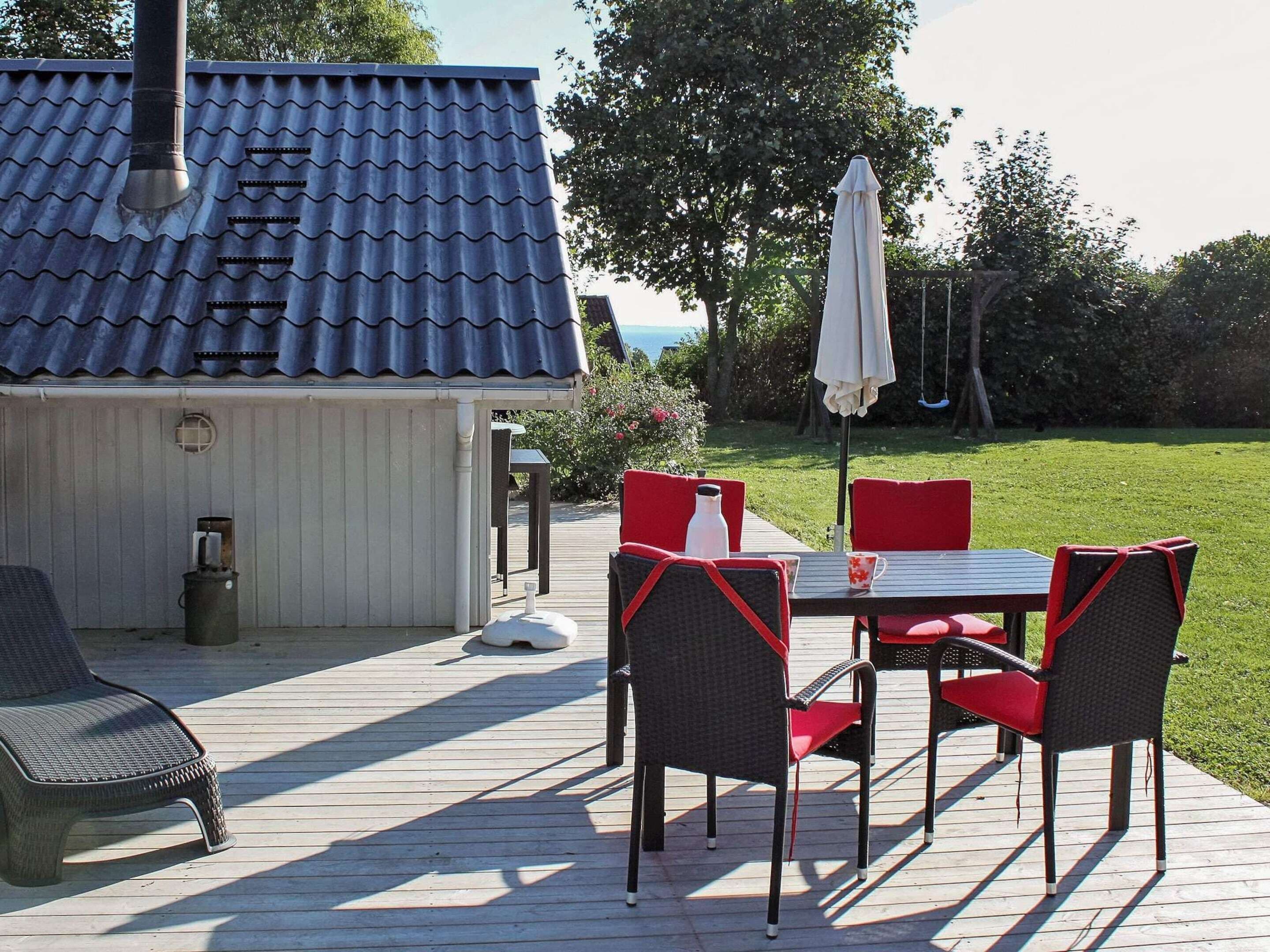 A patio with a table and chairs, a white umbrella, and a small shed with a tiled roof.