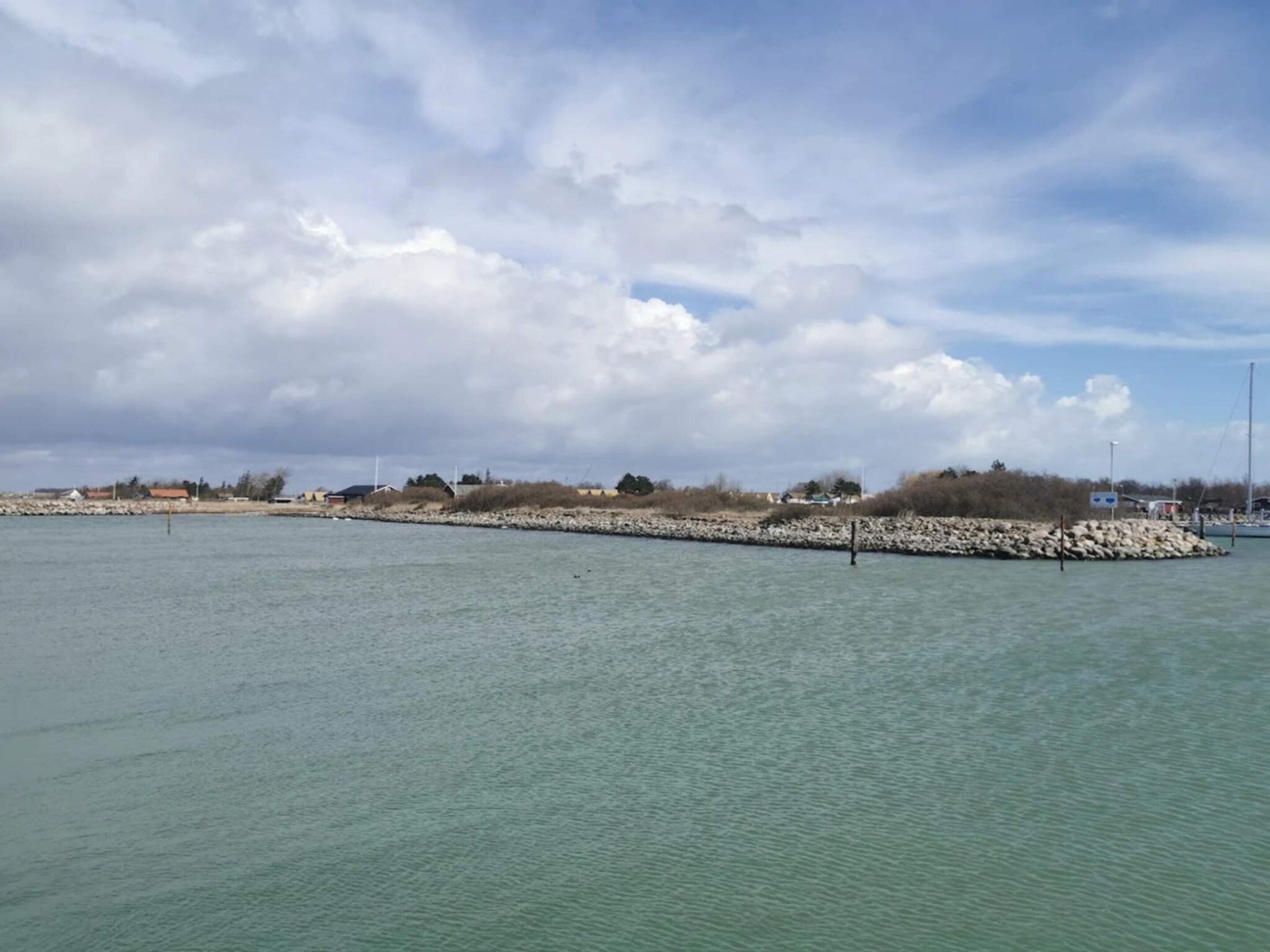 A calm body of water with a rocky breakwater and a distant shoreline with buildings.