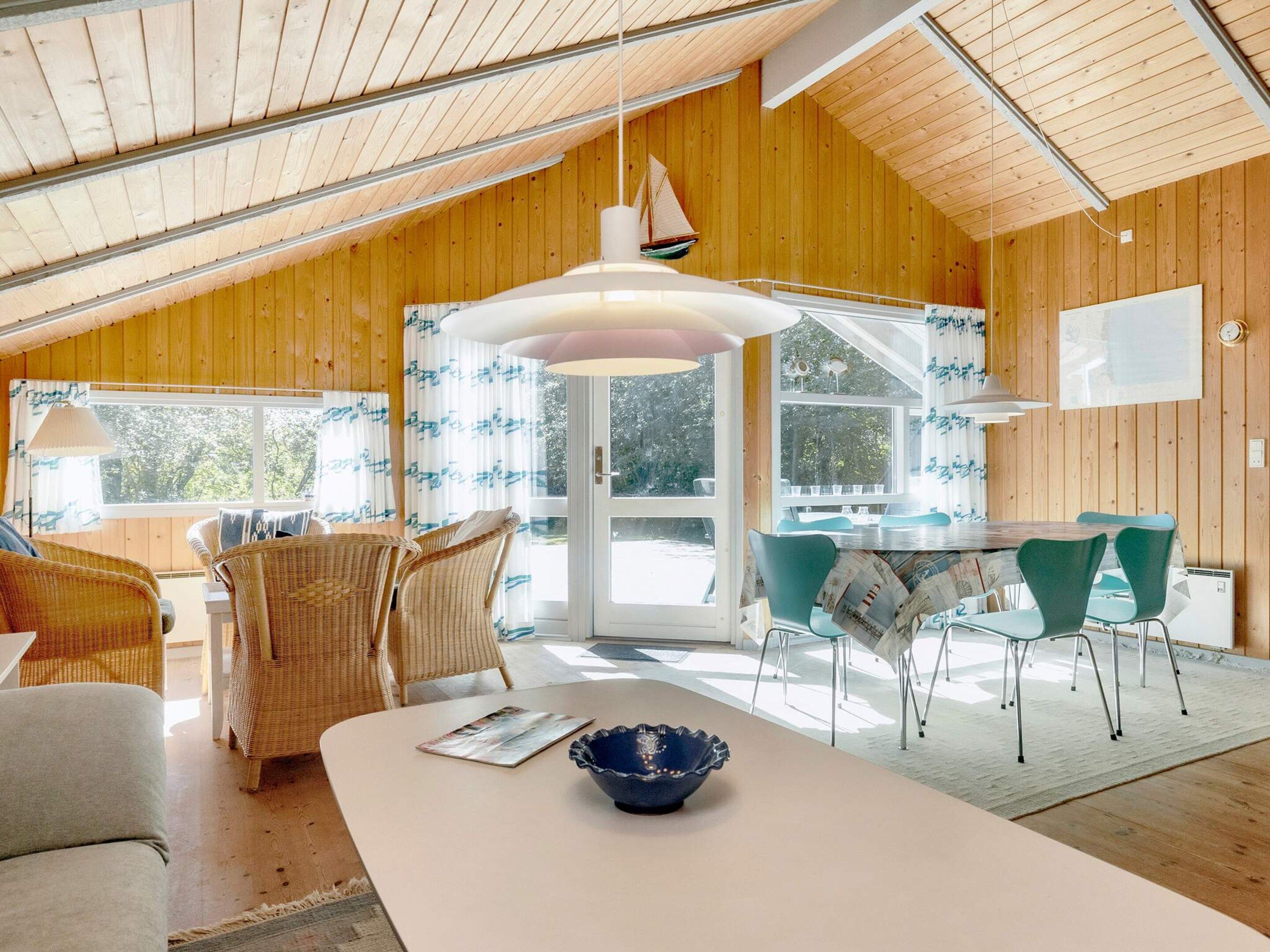 A room with a high ceiling, wooden walls, a dining area with chairs and a table, and a large window.