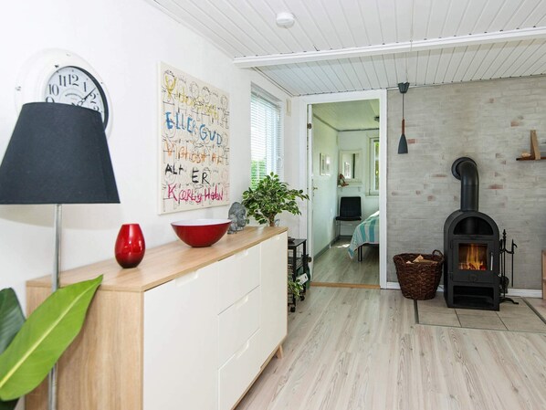 A modern living room with a fireplace, wooden flooring, and a kitchen area with a white cabinet and a red bowl.