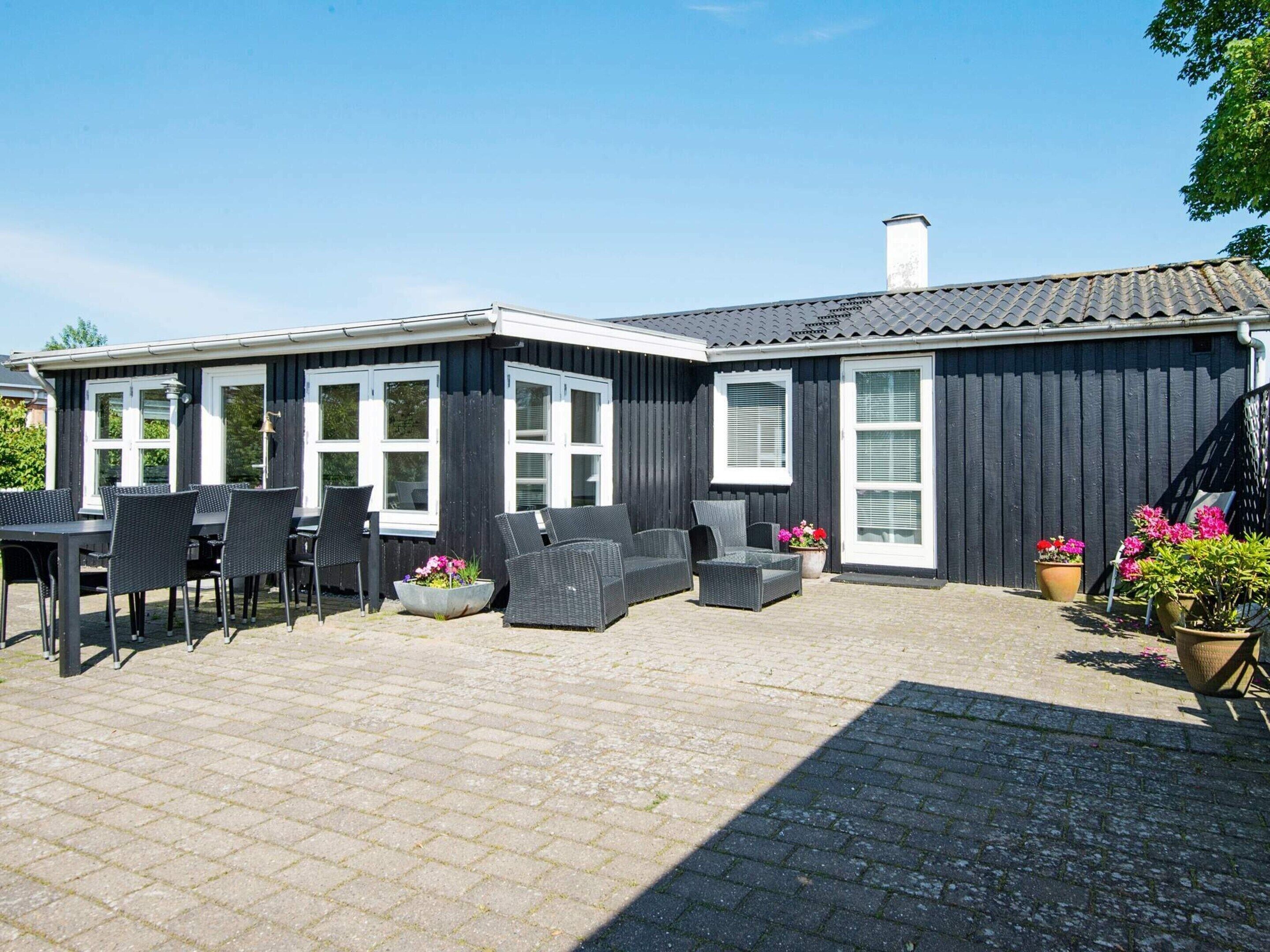 A black building with white windows, outdoor seating, and potted plants.