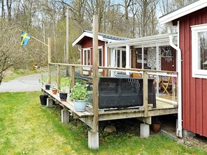 A wooden deck with potted plants, a covered seating area, and a red building with a window. - 7 Person Holiday Home in Allingsas, Sverige (Alingsas)