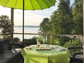 A table with a green tablecloth, two glasses, a book, and a small container, set against a backdrop of a lake and trees. - 7 Person Holiday Home in Allingsas, Sverige (Alingsas)
