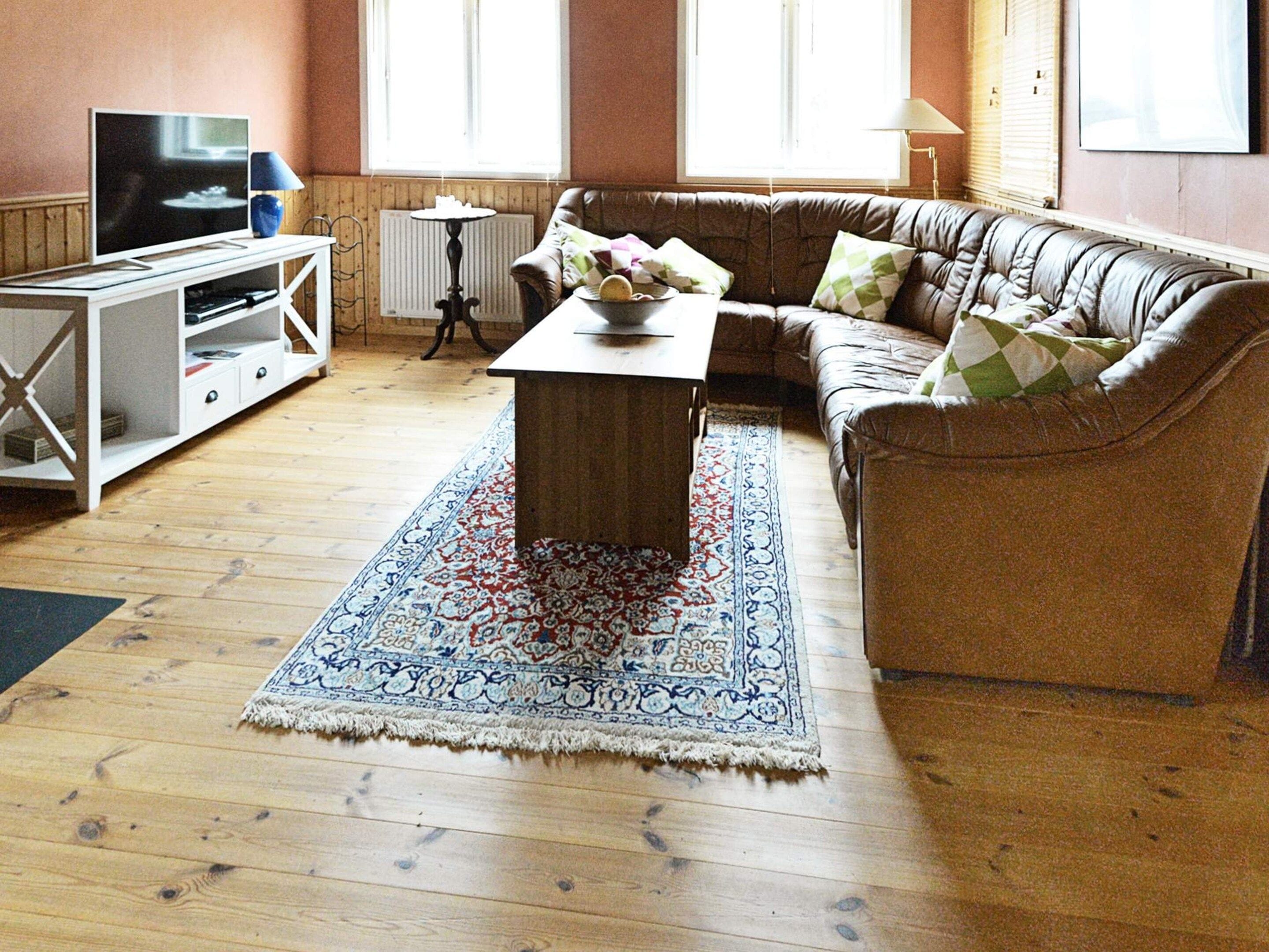 A living room with a brown leather sofa, a wooden coffee table, a TV on a stand, and a patterned rug.
