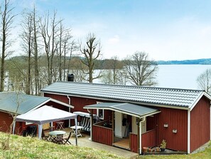 A red wooden cabin with a covered patio, a small deck, and a view of a lake. - 7 Person Holiday Home in Allingsas, Sverige (Alingsas)