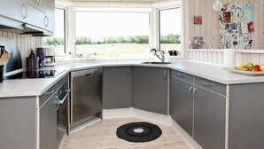 Eine moderne Küche mit grauen Schränken, einem eingebauten Geschirrspüler, einem großen Fenster und Blick ins Freie.