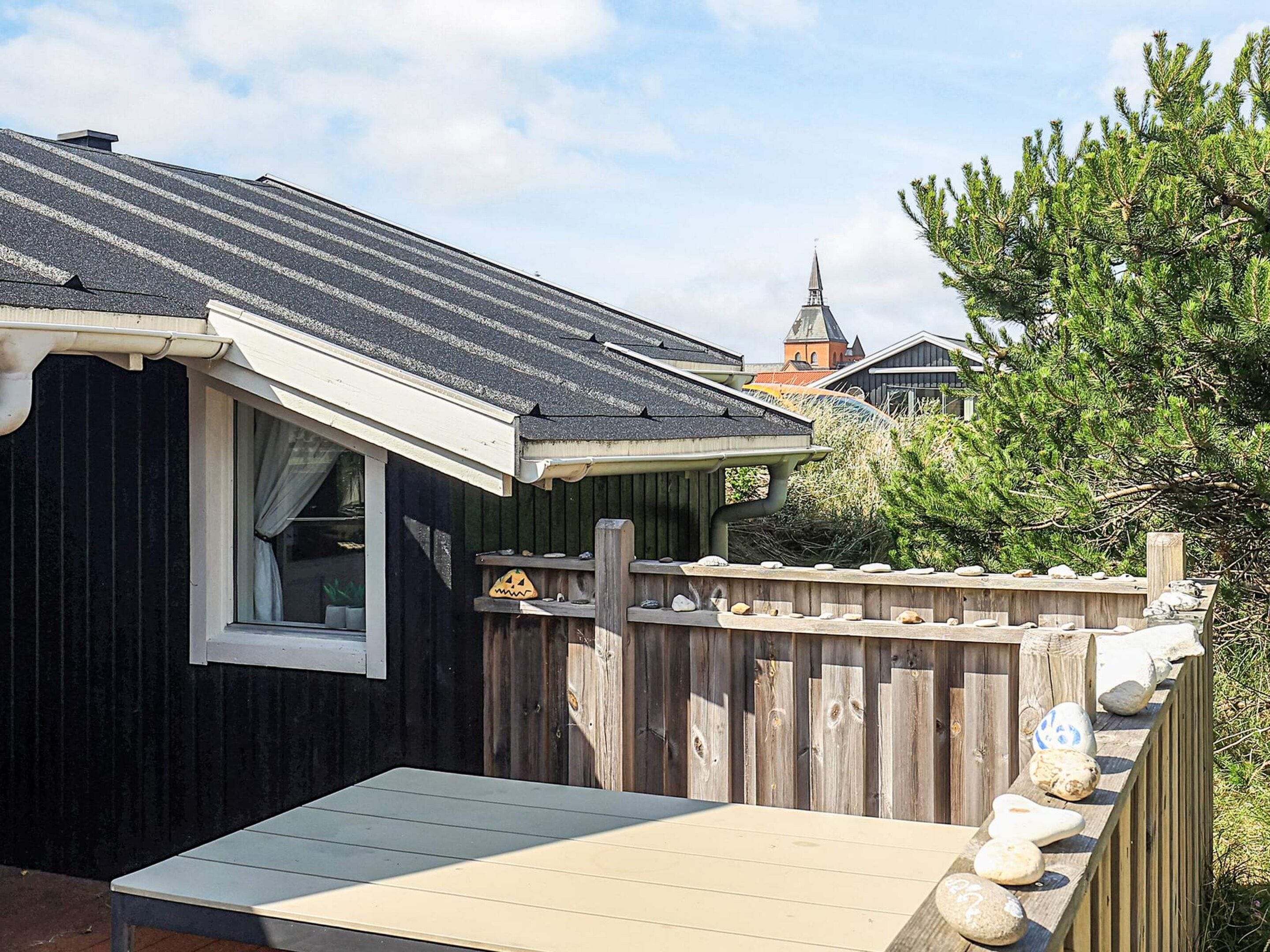 A small wooden cabin with a sloped roof, a window with curtains, and a deck with decorative stones.
