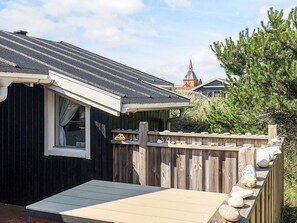 A small wooden cabin with a sloped roof, a window with curtains, and a deck with decorative stones.