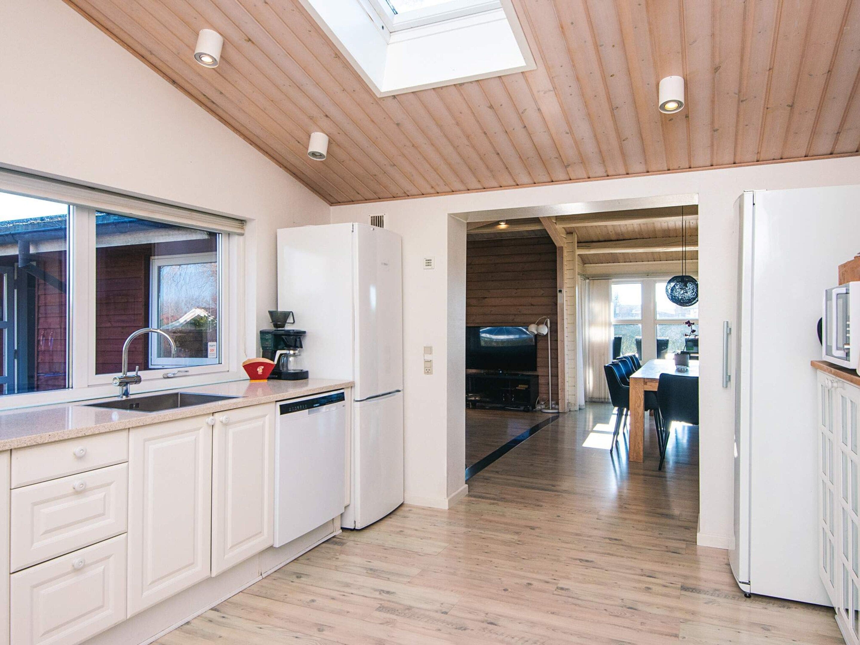 A modern kitchen with a skylight, wooden ceiling, and a dining area with a TV.
