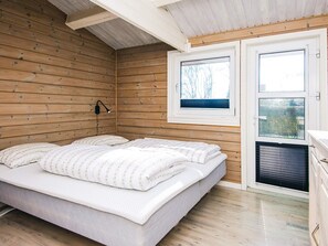A bedroom with a wooden slat ceiling, a bed with white bedding, a window with blinds, and a door with a view of the outdoors. - 4 Star Holiday Home in Juelsminde (Juelsminde)