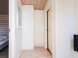 A hallway with a wooden floor, a white door, and a bed with a patterned bedspread.