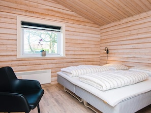 A room with wooden walls, a bed with white bedding, a black chair, a window with a view of trees, and a wall-mounted light fixture.