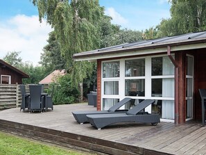 A wooden deck with outdoor furniture, a covered seating area, and a building with large windows.