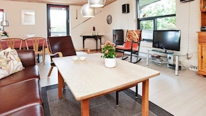 Una sala de estar acogedora con techo de madera, comedor con mesa y sillas, televisor y chimenea.