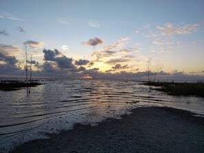 Un paysage côtier avec une étendue d’eau, un ciel dégagé et un coucher de soleil.