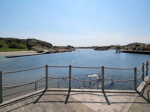 A wooden dock with a rope railing, leading to a calm body of water with rocky outcrops and a clear sky. - Holiday Home in Skärhamn (Skaerhamn)