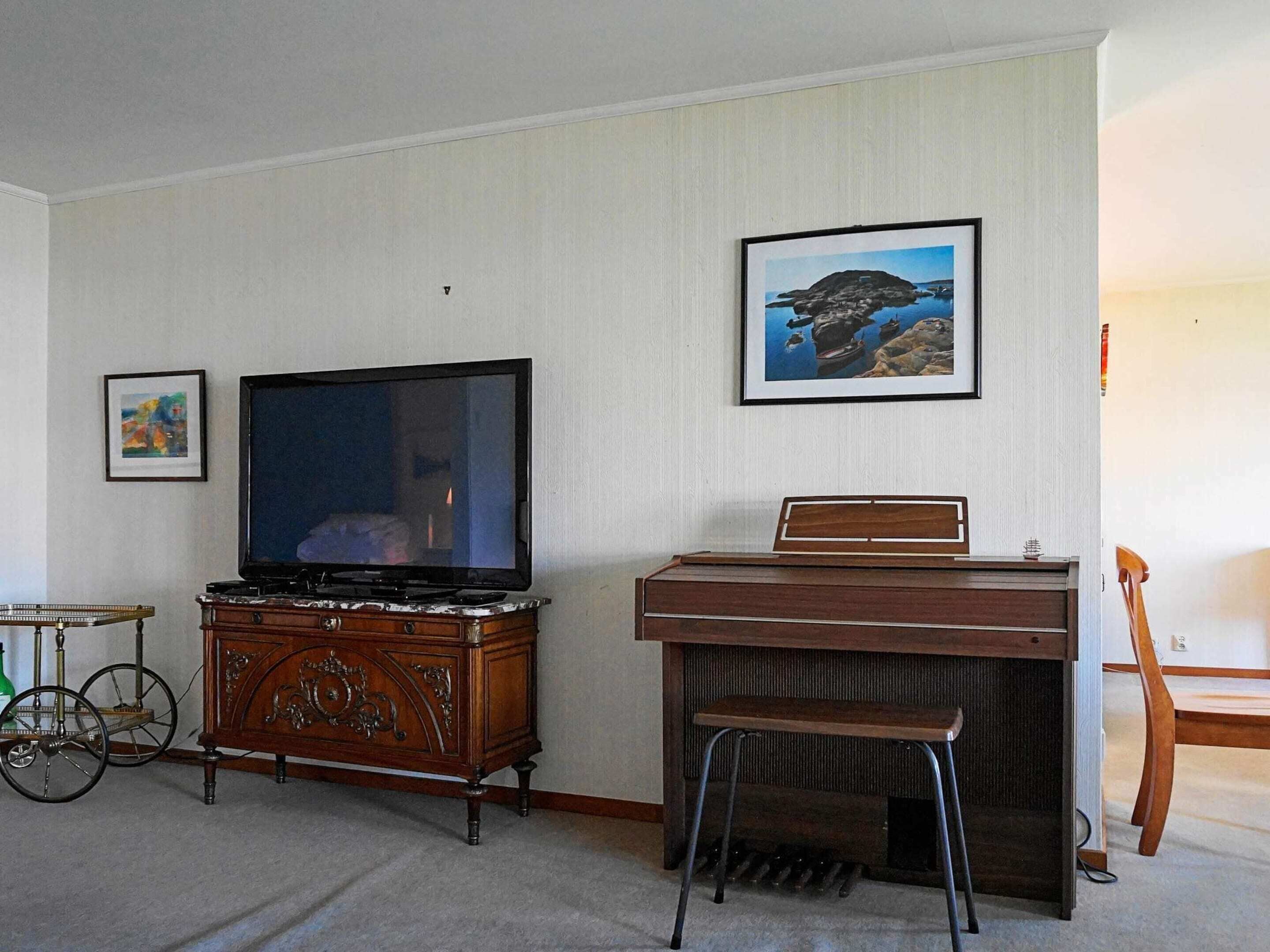 A room with a television on a wooden cabinet, a piano, and a bicycle.