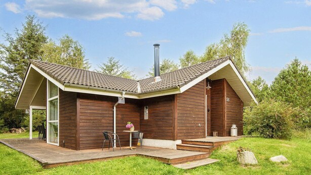 En moderne træhytte med skråt tag, skorsten og en terrasse med udendørs møbler.