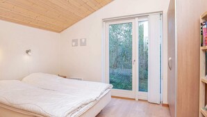 Et soveværelse med træloft, en seng med hvide sengetæger, et sengebord, en vægmonteret lampe og en skydedør af glas, der fører ud til en have.