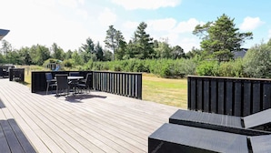 A wooden deck with outdoor furniture, including a table and chairs, surrounded by a black fence and greenery. - 9 Person Holiday Home in Jerup (Jerup)
