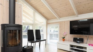 A modern living room with a wood-burning stove, two chairs, a TV, and a white cabinet with electronics. - 9 Person Holiday Home in Jerup (Jerup)