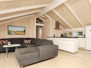 A modern interior with a sectional sofa, a small round table, and a kitchen area with a microwave and cabinets. - 9 Person Holiday Home in Jerup (Jerup)