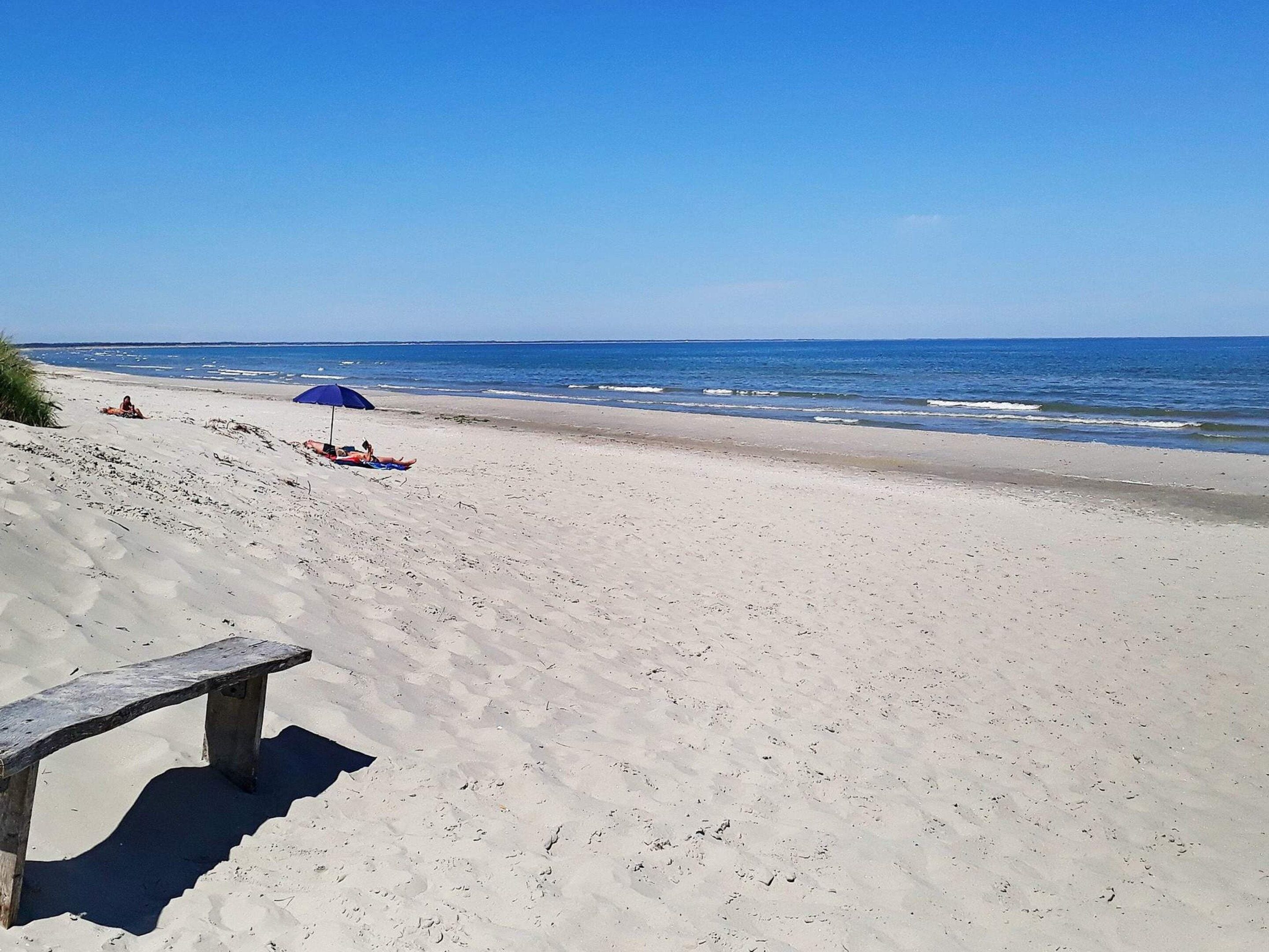 Une plage avec un banc en bois et un parasol bleu.