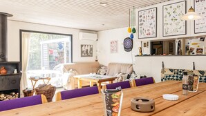 A cozy living room with a sofa, a dining table with chairs, and a kitchen area with a fridge and a hanging light fixture. - 8 Person Holiday Home in Hadsund (Hadsund)