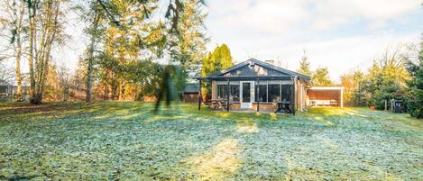 A house with a covered patio, a fenced yard, and a large tree in the background.