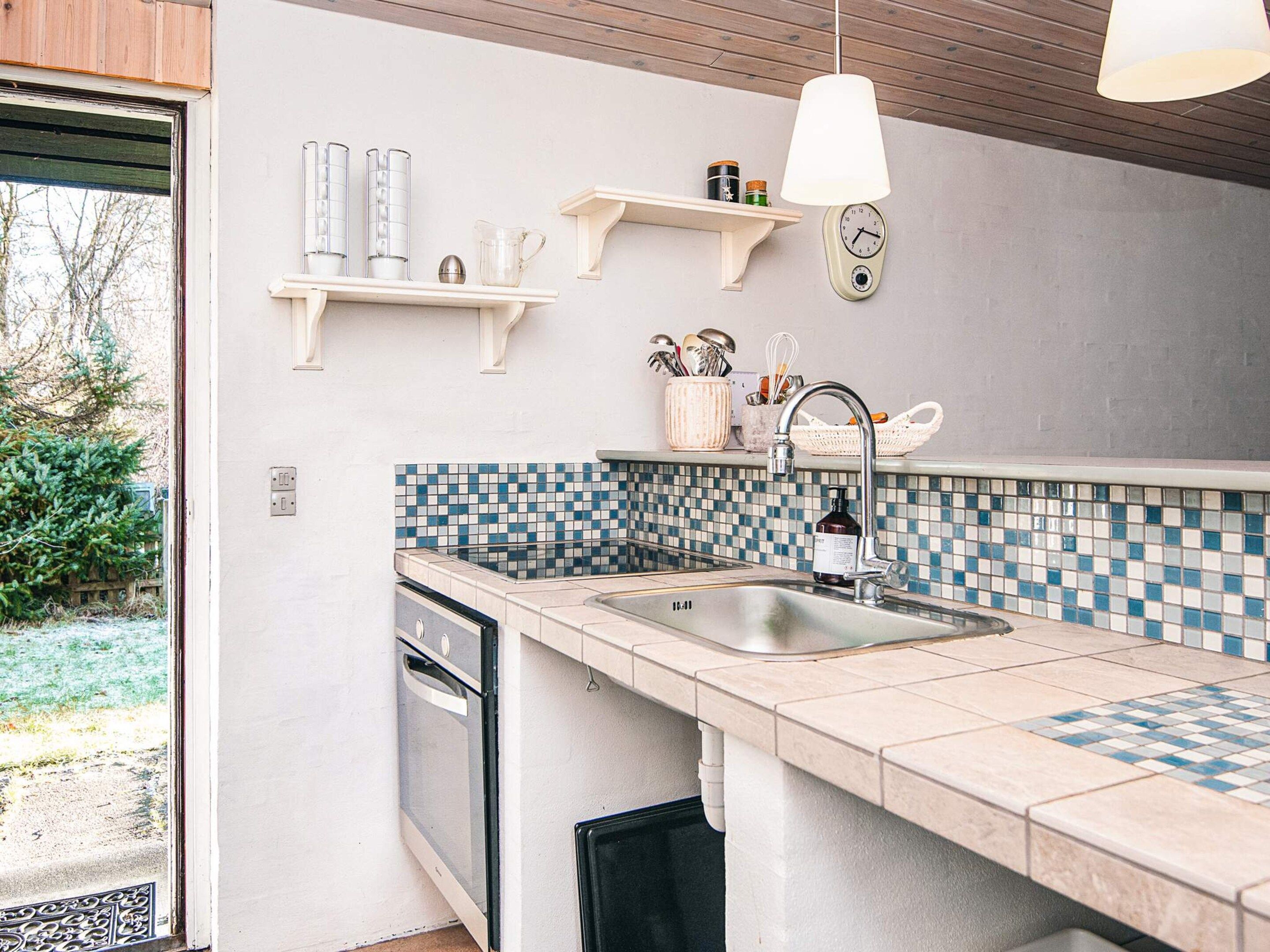 A modern kitchen with a tiled backsplash, a built-in dishwasher, and a hanging light fixture.