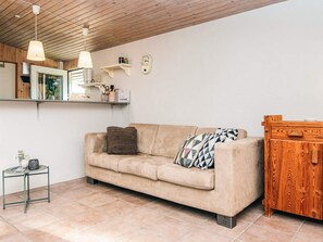 Una sala de estar con un sofá color beige, una mesita auxiliar, un mueble de madera y un techo con vigas de madera.