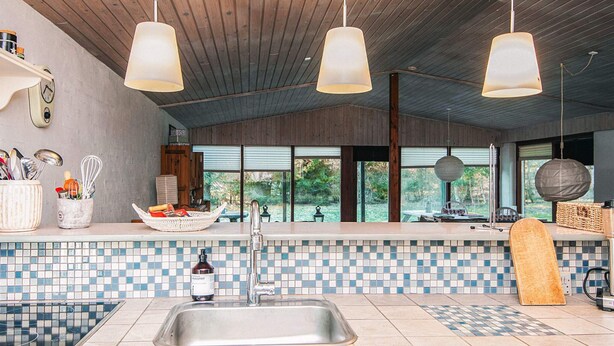 A modern kitchen with a tiled backsplash, a stainless steel sink, hanging pendant lights, and a view of the outdoors through large windows. - 2 Person Holiday Home in Tarm (Tarm)