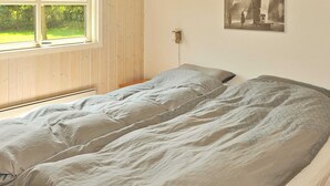 A room with two single beds, a window with a view of greenery, and a wall-mounted light fixture.