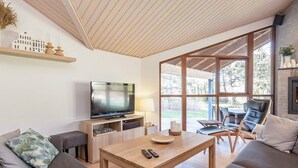 A modern living room with a flat-screen TV, wooden coffee table, grey sofas, and large windows offering a view of the outdoors. - 4 Star Holiday Home in Skals (Skals)