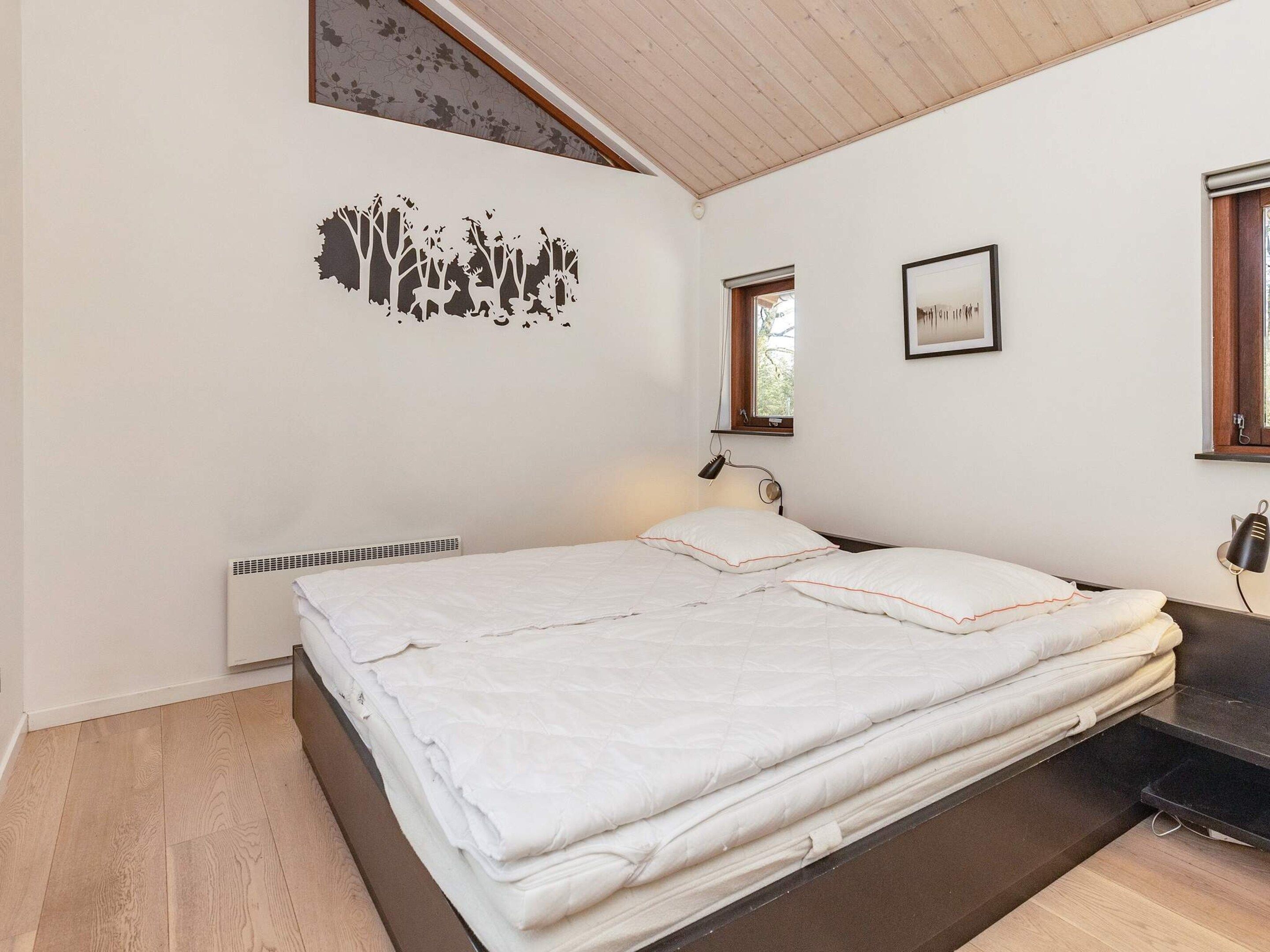 A bedroom with a bed, a wall-mounted heater, a window, and a picture frame.