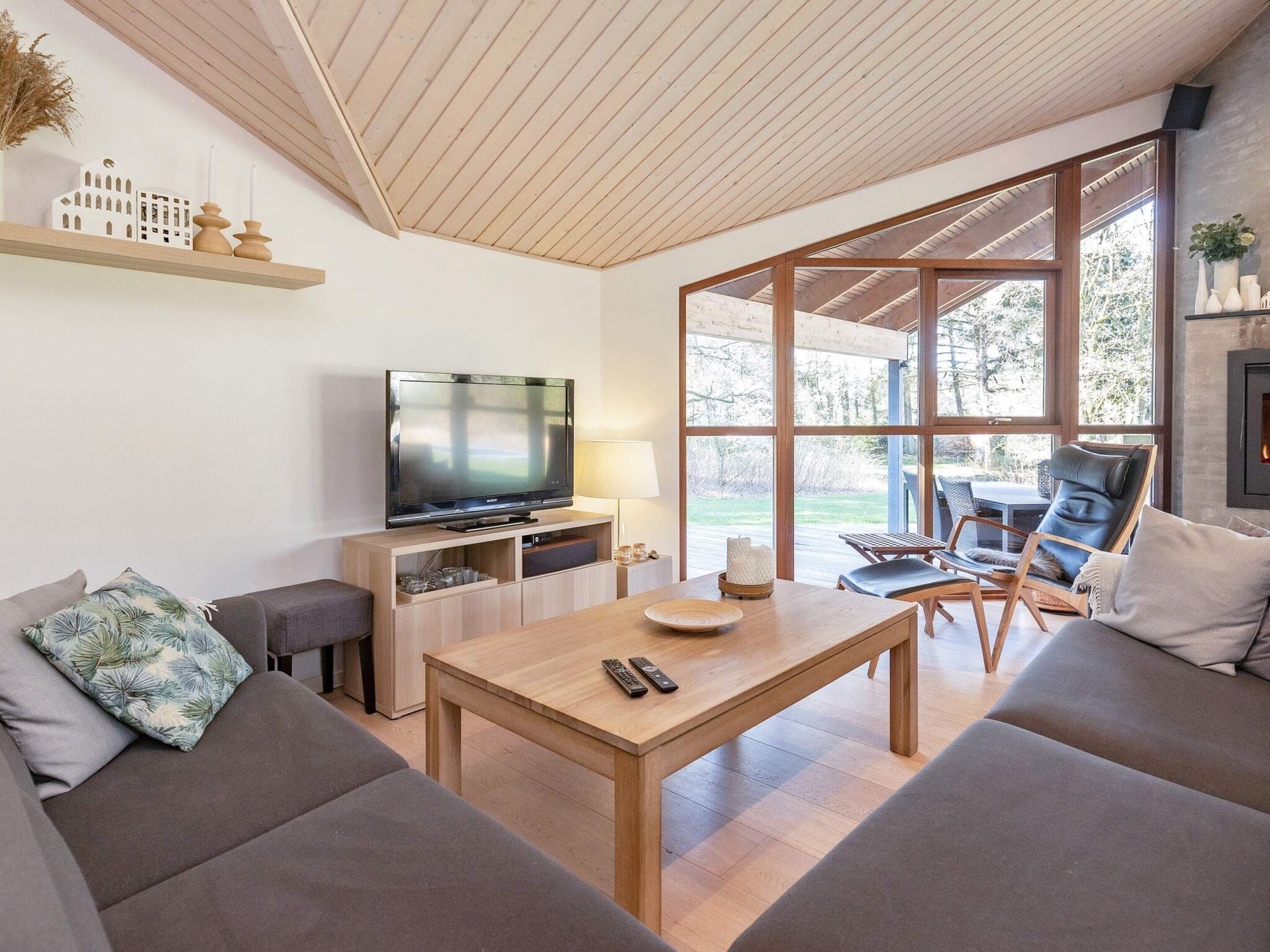 Uma sala de estar moderna com televisão de tela plana, móveis de madeira e grandes janelas com vista para o exterior.