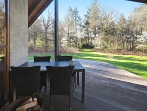 An outdoor patio with a table and chairs, a wooden deck, and a view of a grassy area with trees. - 4 Star Holiday Home in Skals (Skals)