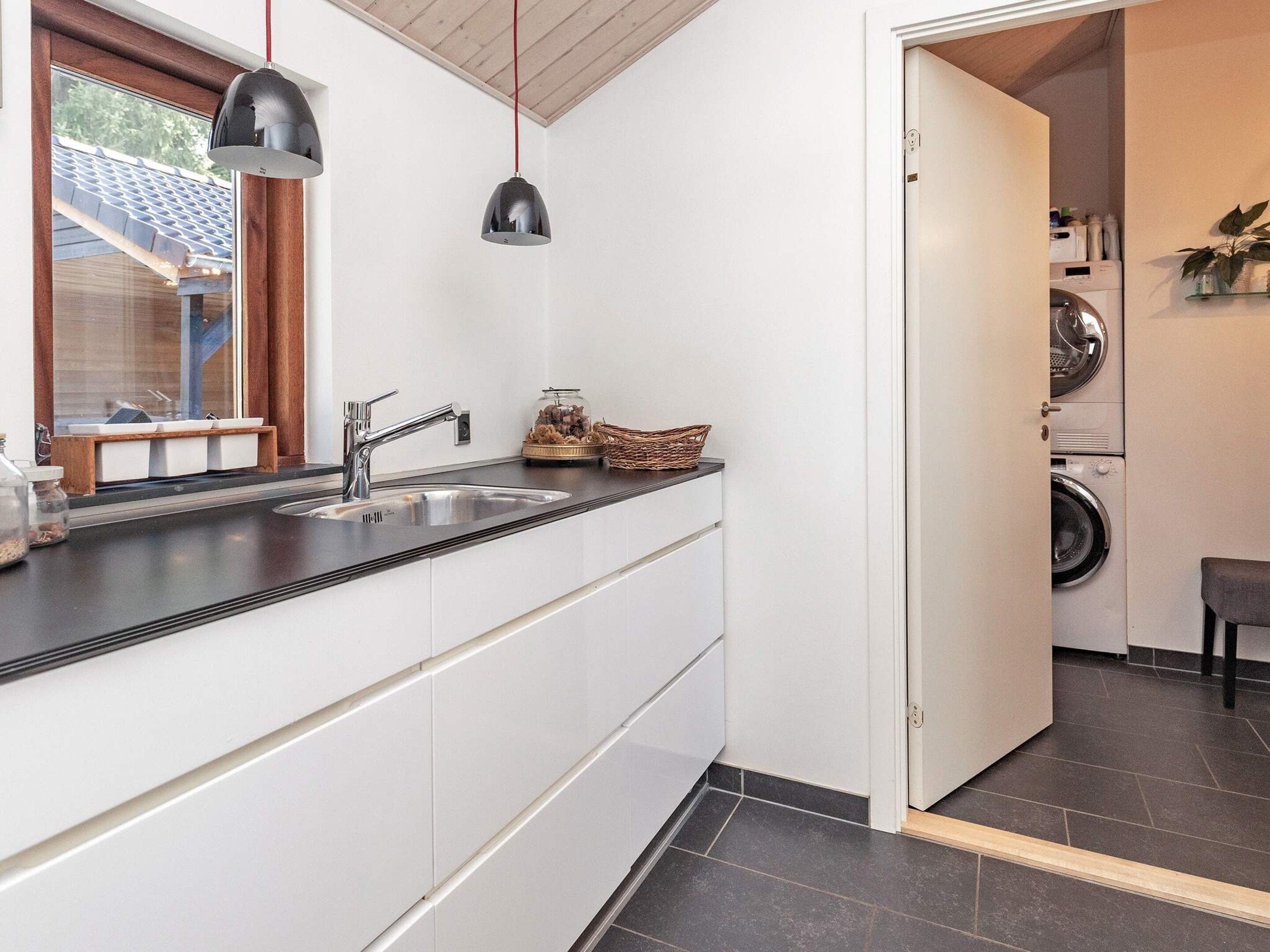 Une cuisine moderne équipée d’un évier, de deux luminaires suspendus et donnant sur une buanderie.