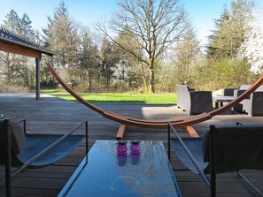 A hammock between two chairs on a wooden deck with a glass table, surrounded by outdoor furniture and trees. - 4 Star Holiday Home in Skals (Skals)