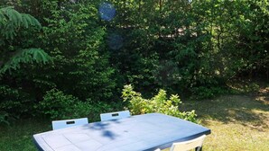 A rectangular outdoor table with four white chairs, set on a grassy area surrounded by dense green foliage. - 6 Person Holiday Home in Hadsund-by Traum (Hadsund)