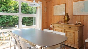 A wooden-paneled room with a dining table and chairs, a vintage brass stove, and a large window offering a view of greenery. - 6 Person Holiday Home in Hadsund-by Traum (Hadsund)