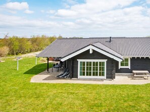 A log cabin with a tiled roof, a covered patio with chairs, and a picnic table.